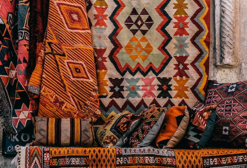 Colorful oriental rugs hanging on wall near sofa with bright cushions with patterns on exhibit in street of old town